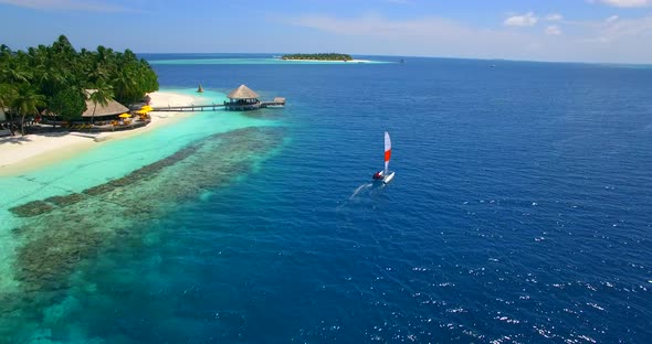 Aerial drone view of a man and woman sailing on a boat to a tropical island.