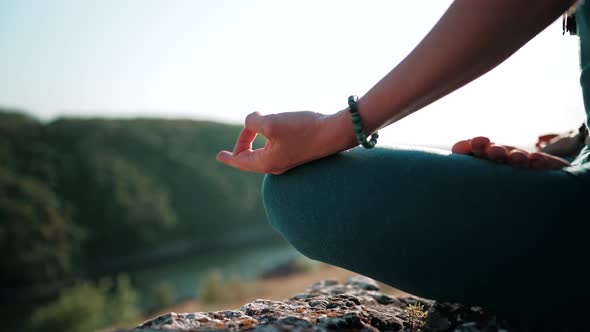 Healthy Woman Sitting in Lotus Pose and Meditating on High Cliff Above River