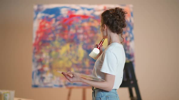 Portrait of a Female Artist Young Woman Stands in the Art Studio and Looks at Her Painting a Painted