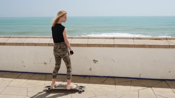A Beautiful Blonde Girl on Skateboard in Summer Hot Day on Seafront