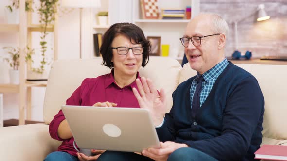 Elderly Age Couple Sitting on Sofa Holding Laptop During a Video Call.