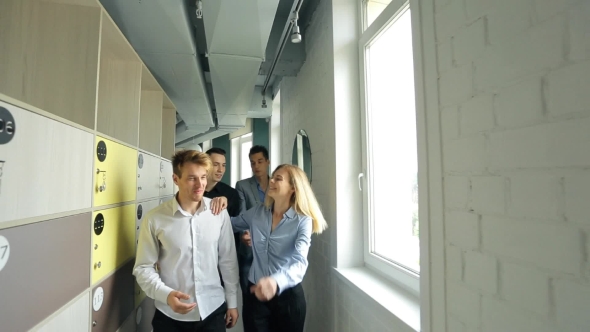 Young Men And Women Praise Each Other And Hug Walking Down Hallway Of Office.