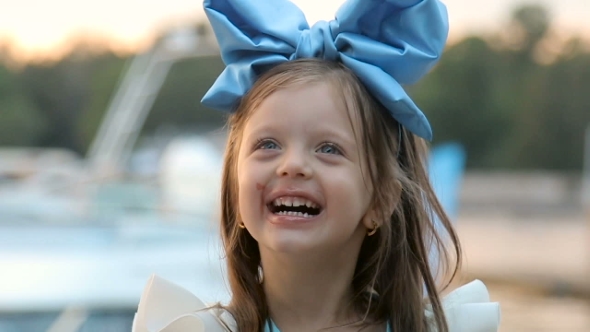 Portrait Of a Little Girl Three Years With The Blue Bow On Her Head, Stands Near The Water