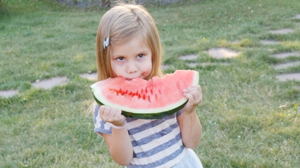 Cute Little Girl Eating Watermelon On The Grass In Summertime