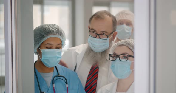 Team of Healthcare Workers in Safety Mask Standing Behind Glass Door Watching Difficult Surgery