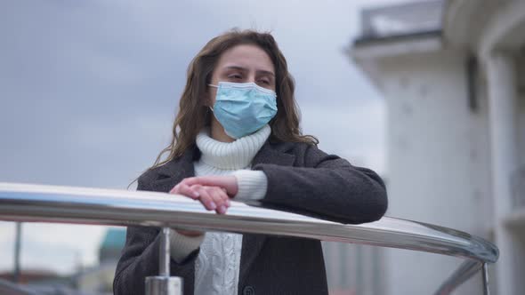 Portrait of Desperate Frustrated Young Caucasian Woman in Coronavirus Face Mask Standing Outdoors at