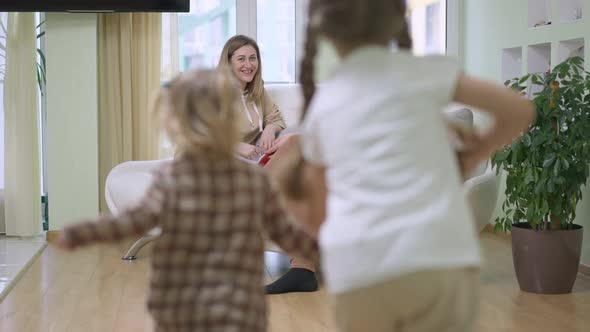 Cheerful Daughters Running in Slow Motion to Couple of Happy Parents Sitting on Couch in Living Room