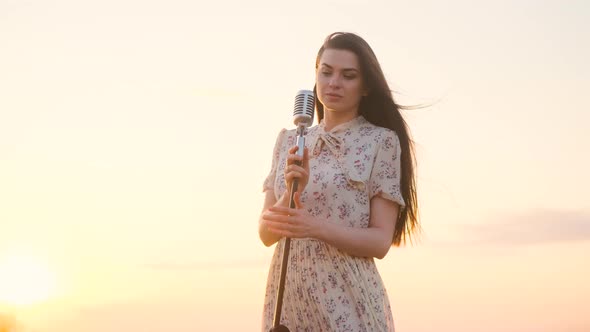 Beautiful Woman in White Dress on Top of Mountain on Edge of Abyss and Sings Song Into Shiny Retro