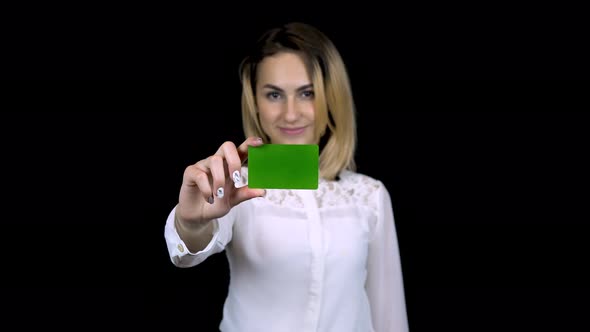 Young Businesswoman in a White Shirt Holds a Bank Card in Her Hand. Isolated Black Background