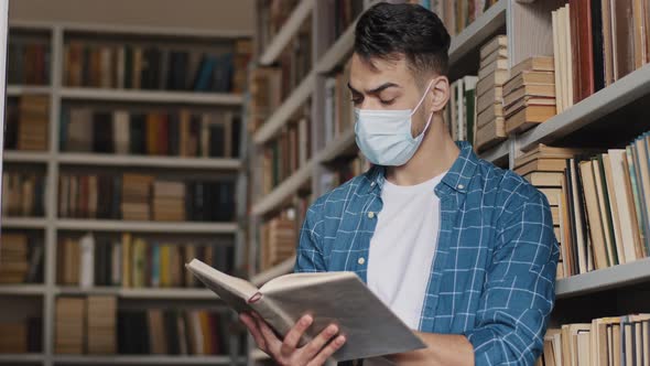 Closeup Hispanic Male Student in Protective Mask Stands Reading Book in Public University Library