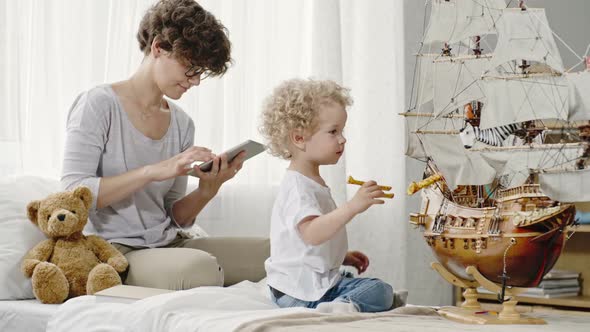 Mother Looking at Tablet while Son Playing