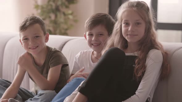 Portrait of Positive Girl and Two Boys Sitting on the Couch Looking at the Camera Smiling