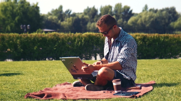 Young Smiling Man Working On Laptop In Sunny Park