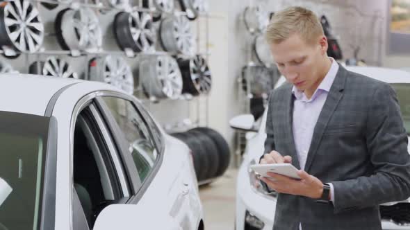 Man Seller with Tablet Shows the Car in the Showroom