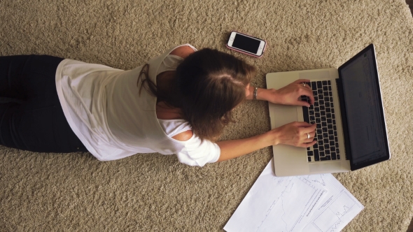Young Brunette Lying On The Carpet And Using Laptop