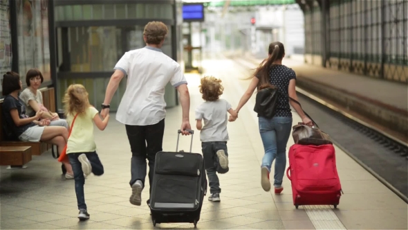 Young Family Of Two Spouses, Son And Daughter, Running To Catch The Train Before It Leaves The