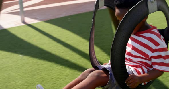 Side view of African American schoolboy playing on a swing in school playground 4k