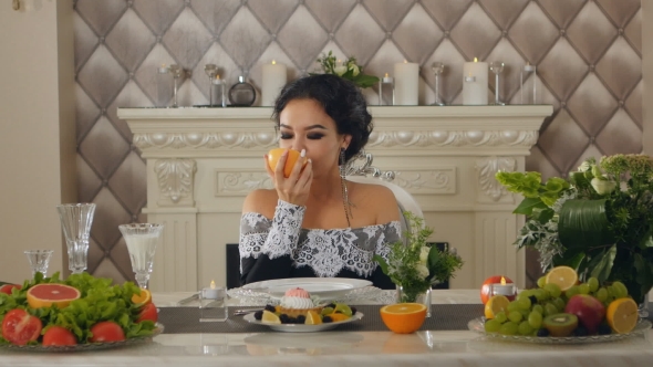 a Woman Sitting At a Table Posing With a Grapefruit In The Hands Of