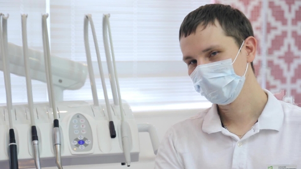 A Young Male Dentist, Disposable Mask, Next To Dental Instrument, Looking Right.