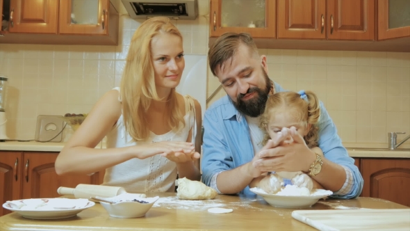 Happy Family Mother, Father And Little Daughter In The Kitchen Preparing Pies From The Test.