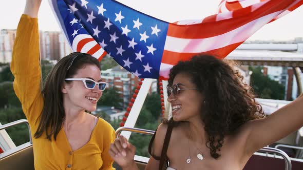 Gorgeous Smartly Dressed Females in Sunglasses are Laughing Holding Flag of USA and Waving It