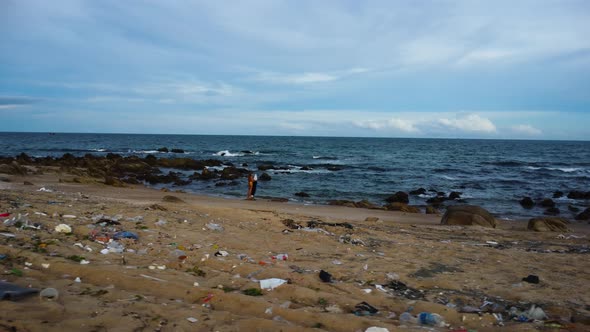 Drone approach female tanned surfer standing on tropical beach with plastic waste garbage trash toxi