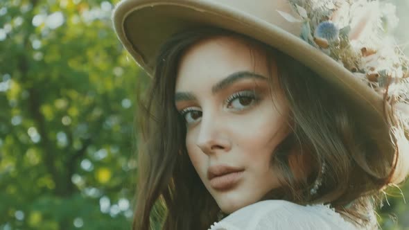 Young beautiful woman in white dress and brown hat posing. Attractive fashion model with loose hair.