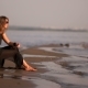 Girl In a Black Dress And Sunglasses Sitting On a Rock On The Beach And Throwing a Pebble Into The - VideoHive Item for Sale