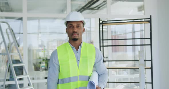 African American Engineer in Hardhat and Vest Posing on Camera with Blueprint