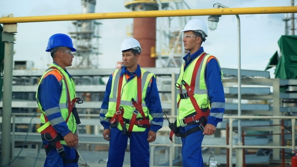 Three Workers In Production Plant As Team Discussing, Industrial Scene In Background