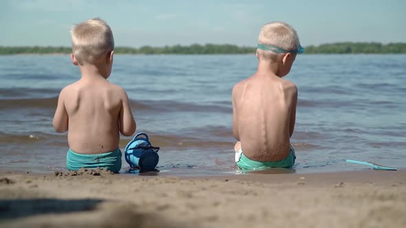 Two brothers sit at the water's edge and play their childish games.