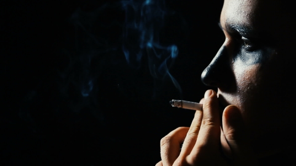 Man With Black Makeup Smokes a Cigarette On a Black Background.