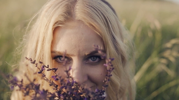 Girl Sitting In The Grass And Smelling a Flower