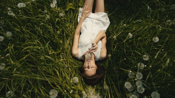 Girl Blowing On a Dandelion Lying On Sunny Meadow