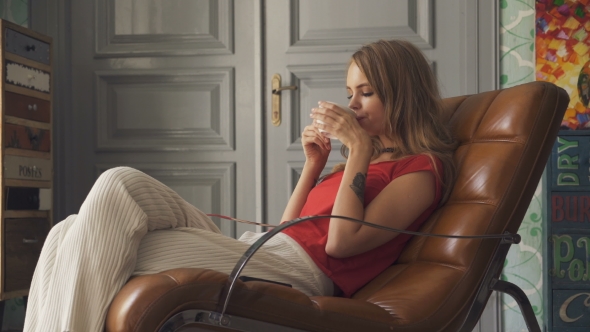 Young Woman With Cup Of Tea Sitting On Armchair At Home.