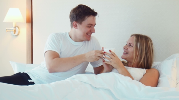 Man Bring a Cup Of Tea Or Coffee To Woman Sleeping In Bed