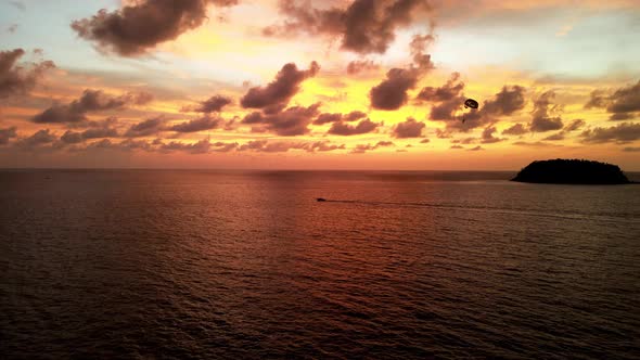 Aerial View Of Parasailer Being Pulled By Boat Against Golden Orange Sunset Skies Over Tropical Wate