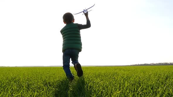 A Happy Child Runs Across a Green Meadow, Holding a Plane in His Hand and Launches It Into the Sky