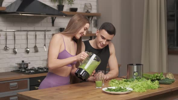 loving couple of athletes preparing healthy drink, smiling woman pouring detox smoothie in glass.