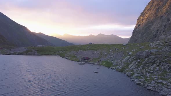 Aerial view of peaceful mountain lake at sunset with dramatic purple and red sky over distant peaks.