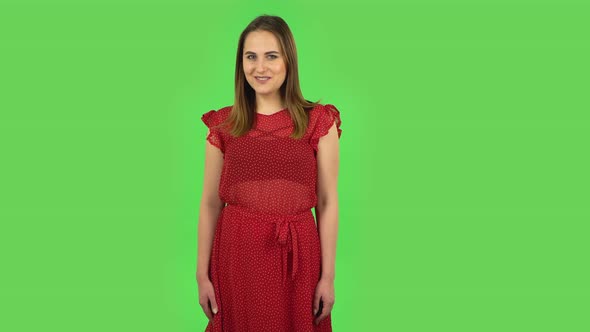 Tender Girl in Red Dress Is Coquettishly Smiling While Looking at Camera. Green Screen