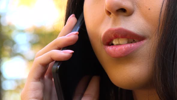 A Young Asian Woman Talks on A Smartphone in A Park