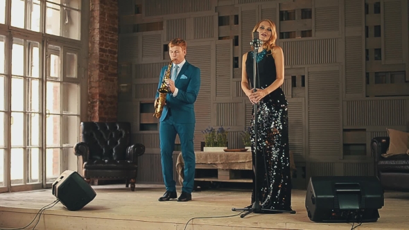 Jazz Vocalist in Glowing Dress and Saxophonist in Blue Suit Perform on Stage.