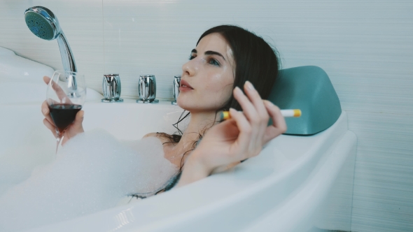 Girl Drink Red Wine In Bath Full Of Foam. Smoking Electronic Cigarette. Smile