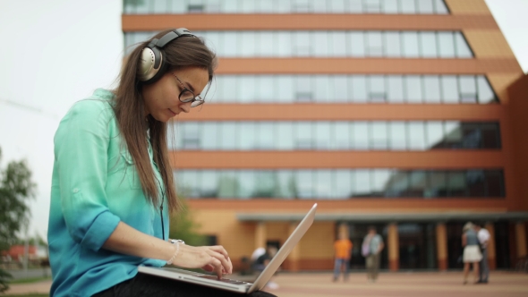 Girl Listening To Music On Headphones And Typing On a Laptop Keyboard.