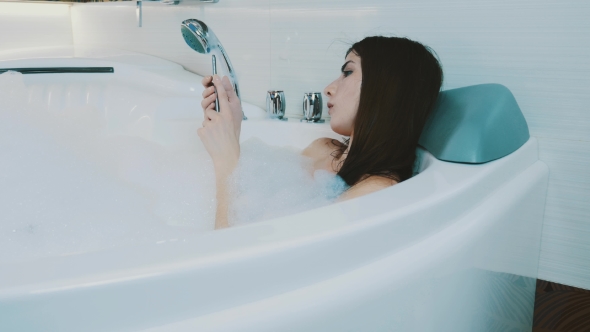 Brunette Girl Taking Bath Full Of Foam. Tap In Smartphone. Relax. Resting.
