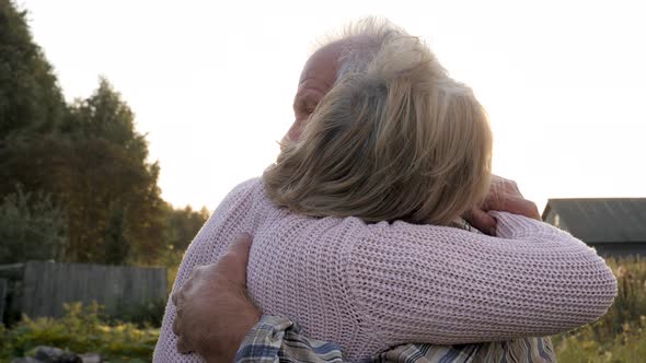 Elderly Couple In Love Hugs In Park Against Of Sunlight At Sunset At Summer Fall