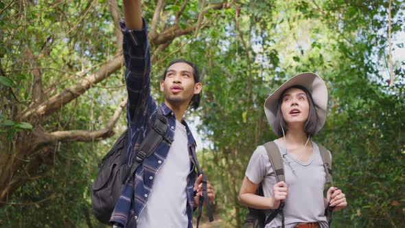 Young Asian man and Caucasian woman friend traveling in the forest together walking with happiness.