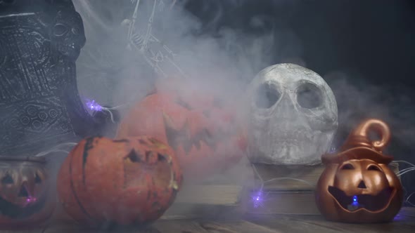 Smoke Is Blowing Over Skull and Halloween Pumpkins Standing at the Table