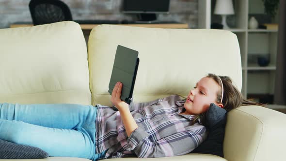 Little Girl Lying on the Couch Using Her Tablet